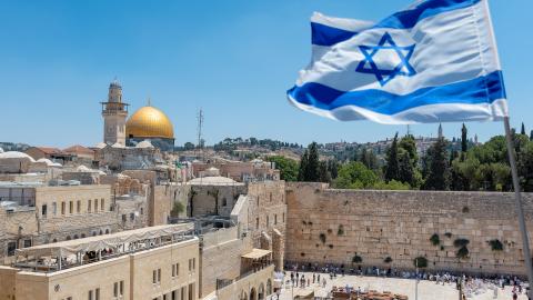 An Israeli flag blows in the wind from an elevated view of the Western Wall. Jewish orthodox believers read the Torah and pray facing the Western Wall, also known as Wailing Wall or Kotel in Old City in Jerusalem, Israel. It is small segment of the structure which originally composed the western retaining wall of the Second Jewish Temple atop the hill known as the Temple Mount to Jews and Christians.