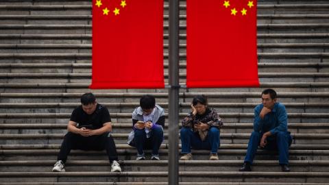 People sit on the steps under Chinese national flags on October 5, 2024, in Chongqing, China. (Cheng Xin via Getty Images)